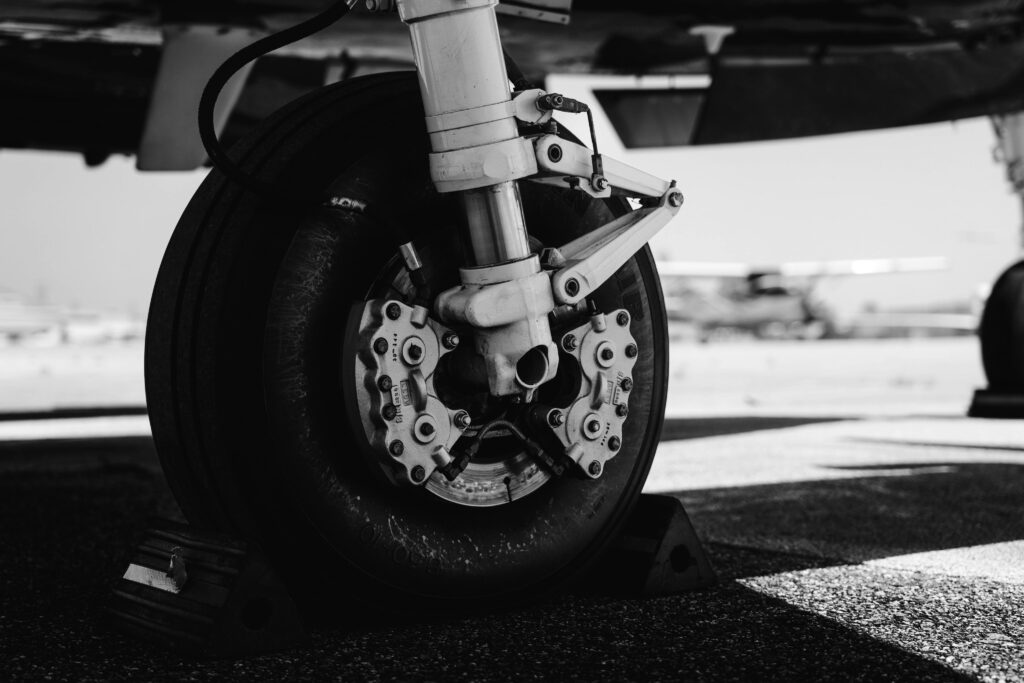 Detailed black and white shot of an airplane landing gear on tarmac, showcasing mechanical components.